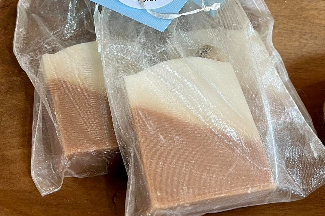 391768876_729025402582621_3506378943368989339_n Handmade natural soap bars packaged in clear organza bags, showcasing a creamy beige and light brown color gradient, displayed on a wooden surface. Ideal for gifting or personal use.
