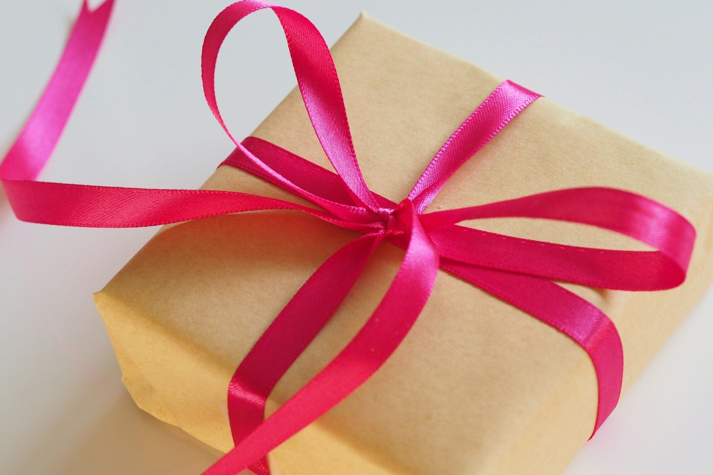 image-asset (4) Gift-wrapped package with a brown paper exterior and a vibrant pink satin ribbon tied in a bow, ideal for celebrations and special occasions.